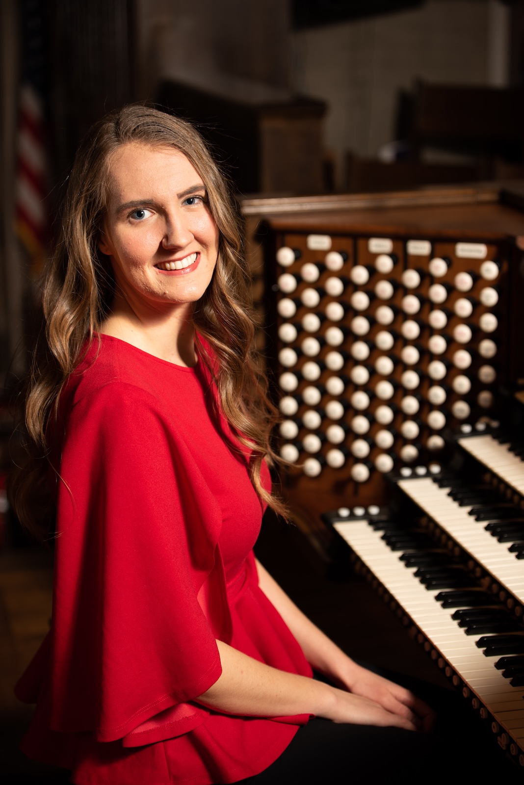 Audrey Pickering in a red dress sitting at the console of a pipe organ