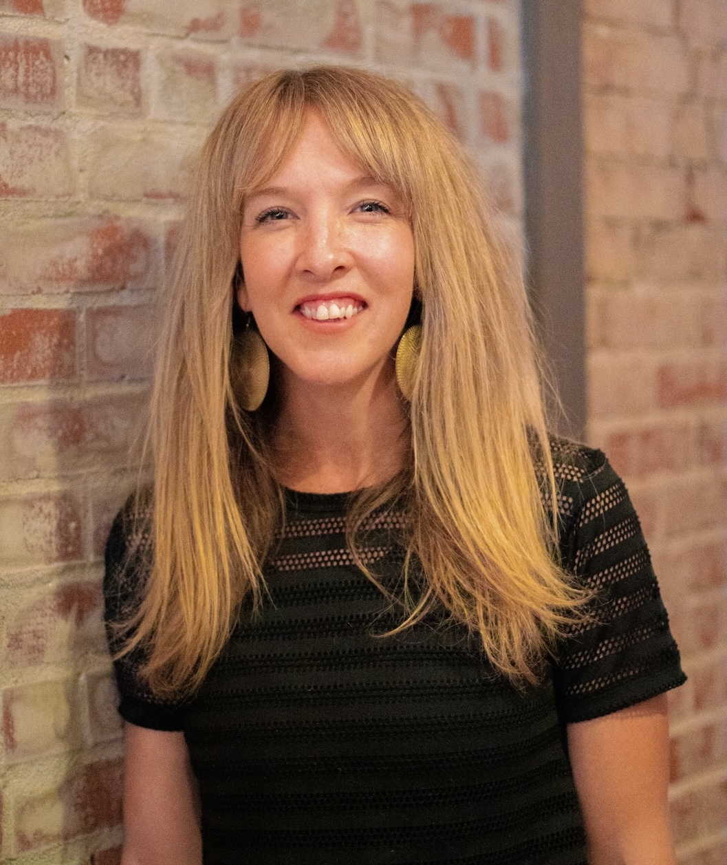 Casey Ward leans against a brick wall in a striped black shirt.