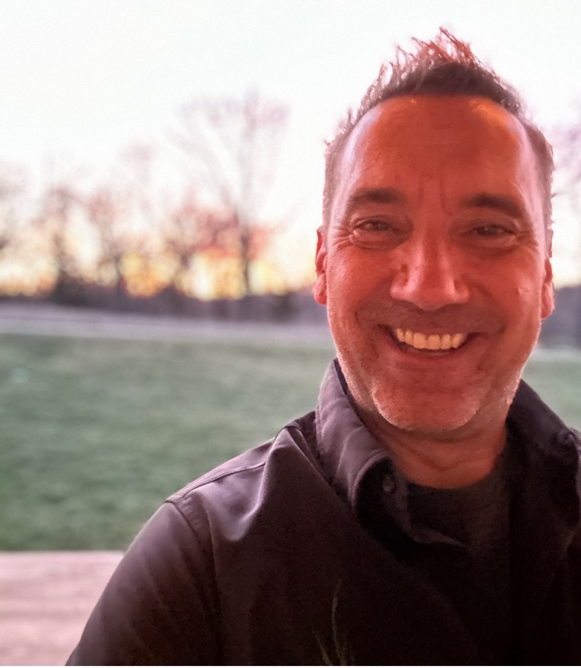 a man in a dark shirt stands in front of an sunset