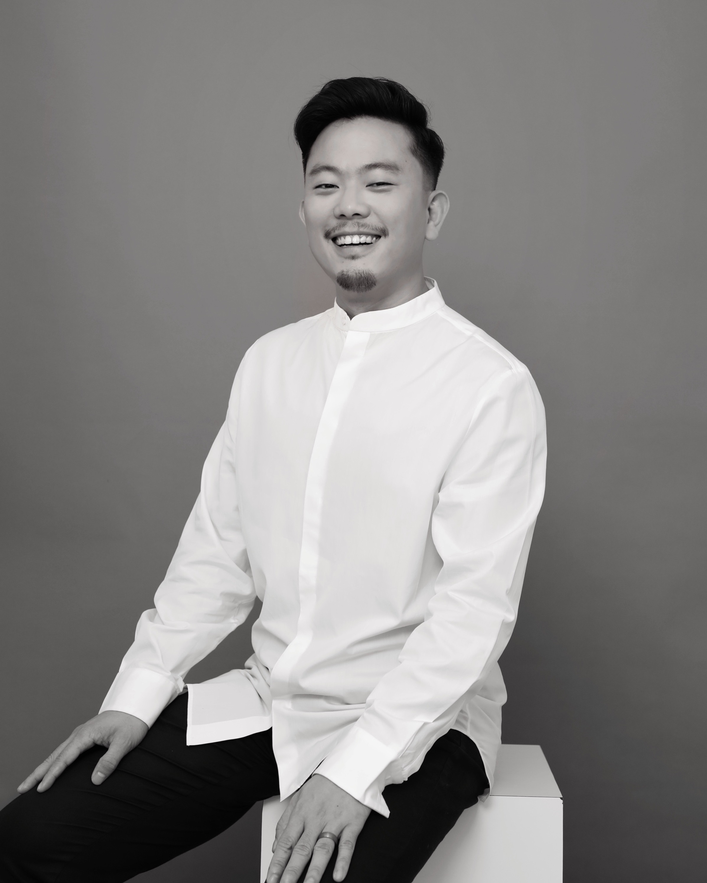 a black and white image of a man with a mustache and beard in a white shirt sitting and smiling