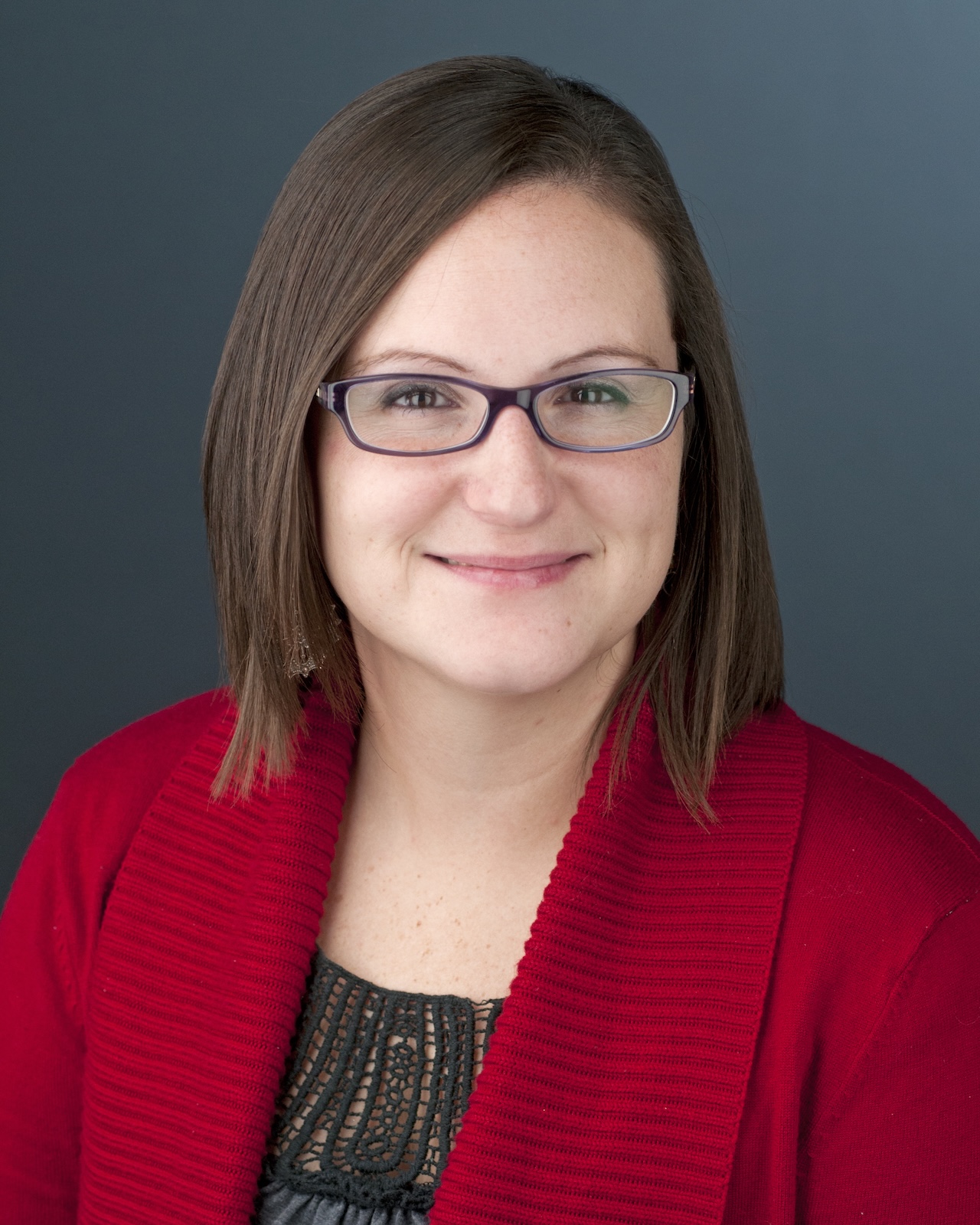 a woman with brown shoulder length hair and glasses in a red top