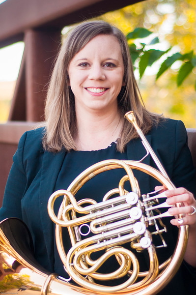 A woman with long hair holding a french horn in a green top