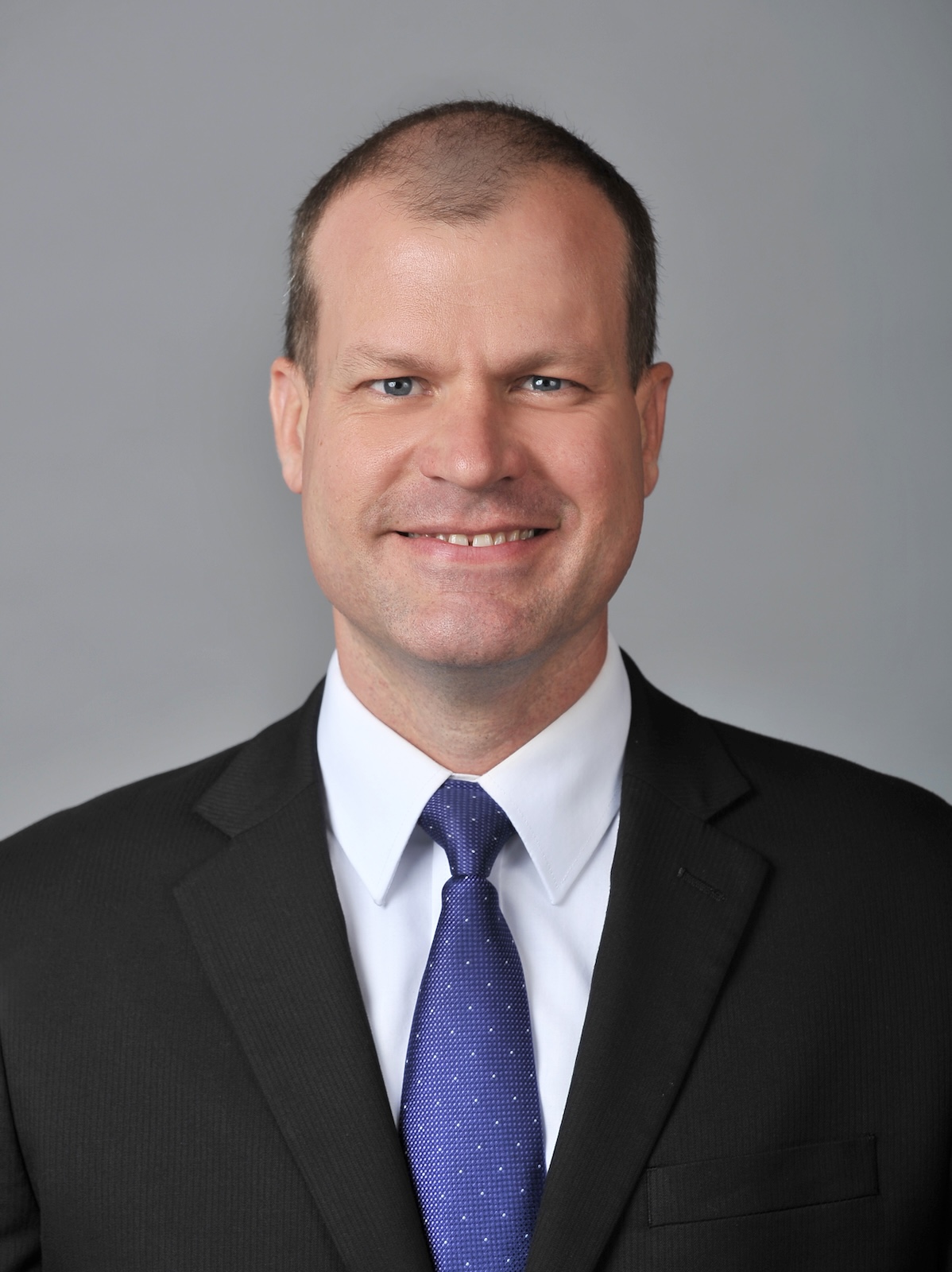 a man in a blue suit smiles in front of a grey background