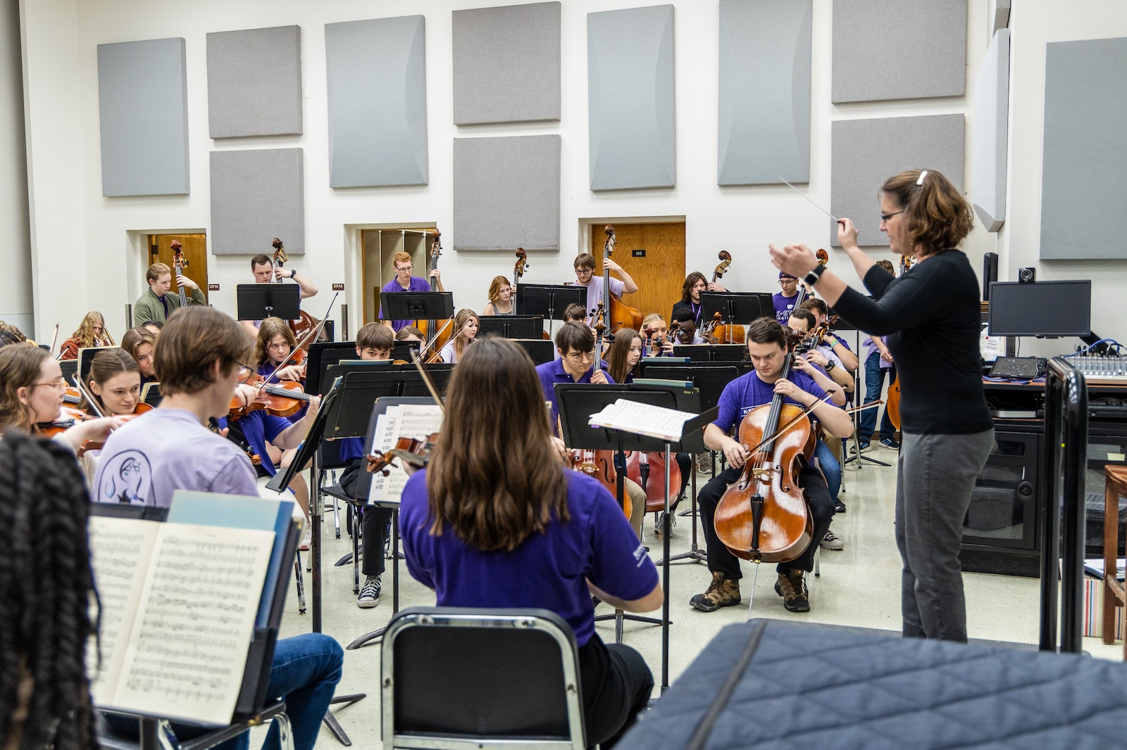 orchestra rehearsal in a classroom with conductor holder her hands high.