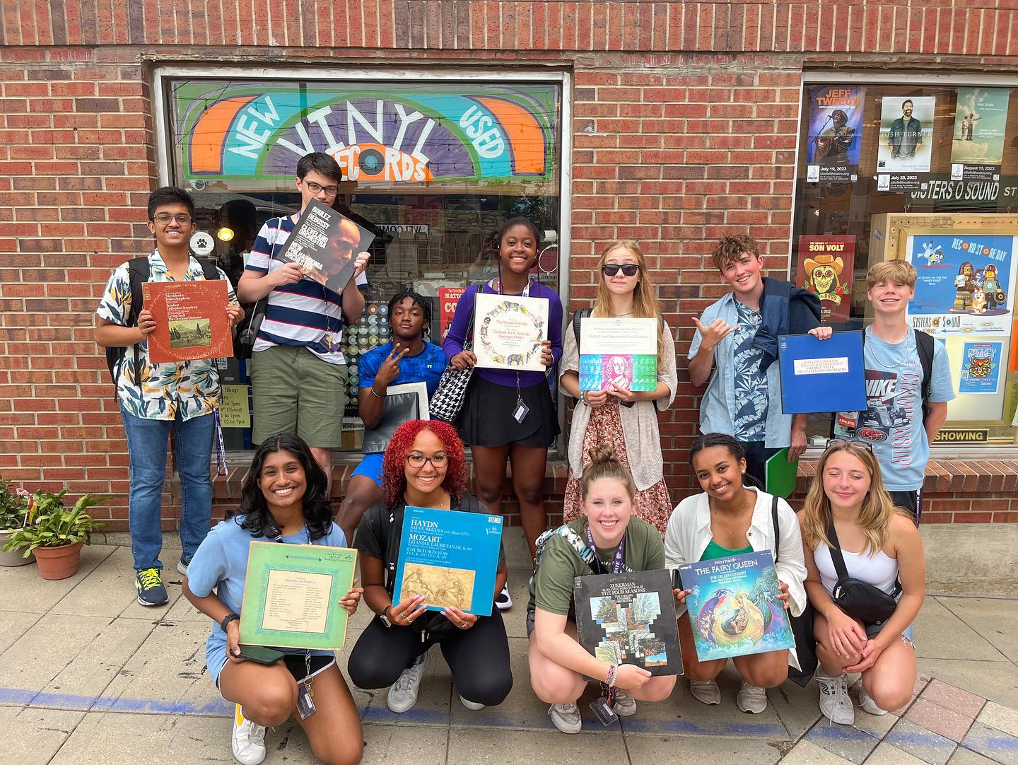 students holding record sleeves outside of a record shop