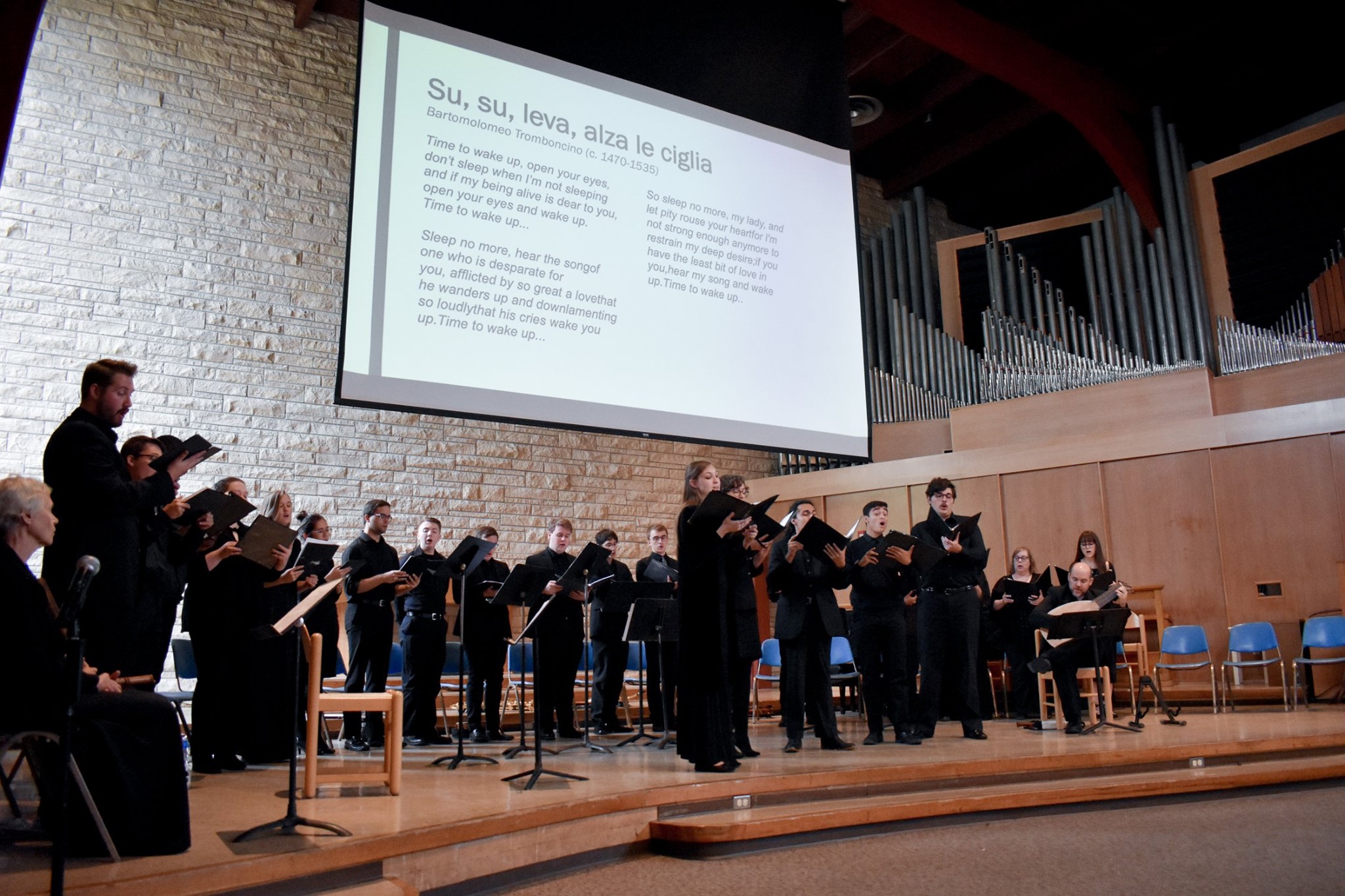 singers stand on stage with a screen projecting song translations above them