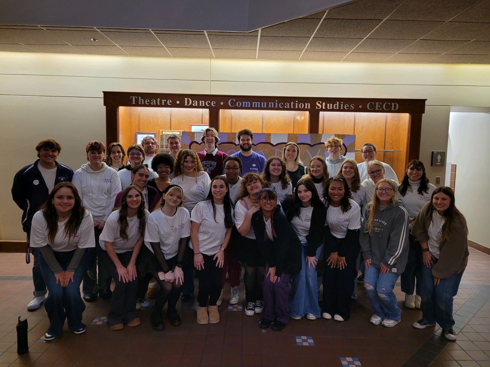 a group of 30 students stand infront of a bank of backlit shelves.