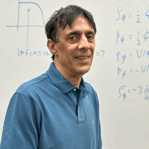 Bharat Ratra in front of white board covered with equations