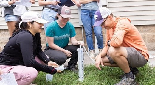 students gathered outdoors near house and working with water testing equipment