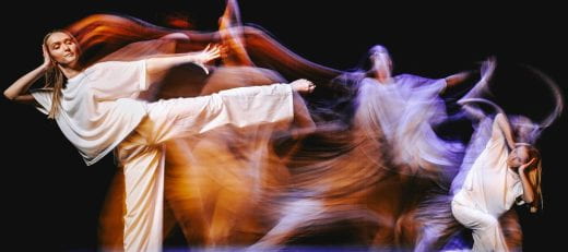 artistic photo of Abbey Griffin dancing in loose white outfit and black background