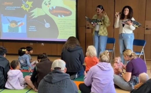 2 K-State students read story in front of group of small children with screen showing images from book
