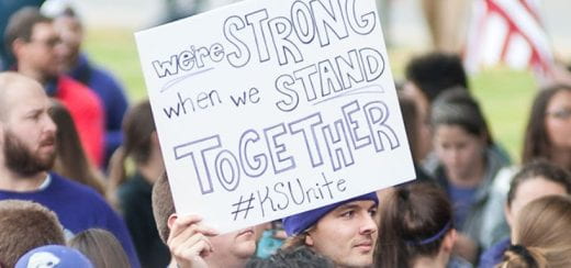 Image of K-Staters gathered and one person holding a sign that says "We're strong when we stand together #KSUnite"