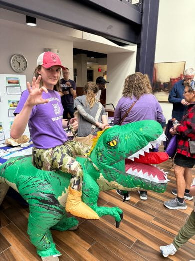 photo of geology student volunteer costumed like he's riding a dinosaur at Open House