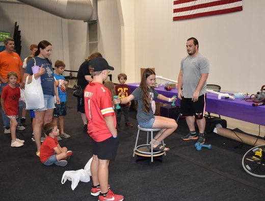 Kids visit K-State Physics exhibit and one is spinning on a stool and holding hand weights