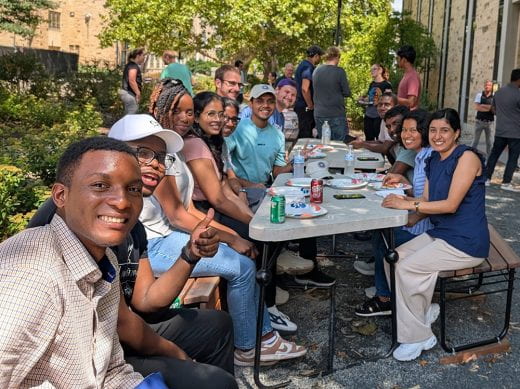 About a dozen men and women smile at camera during picnic