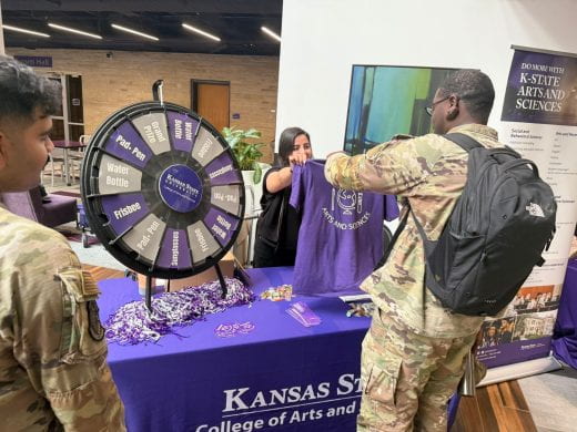 Student in military uniform receives prize t-shirt from Arts and Sciences student ambassador at 2025 Arts and Sciences Discovery Expo