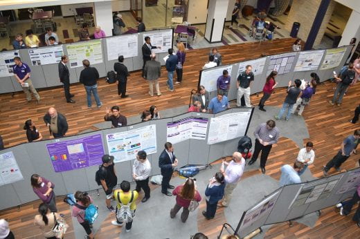 high view of rows of students near their research posters talking with visitors