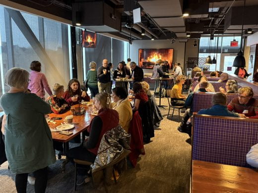 roomful of chatting party guests with cozy fireplace on TV in background