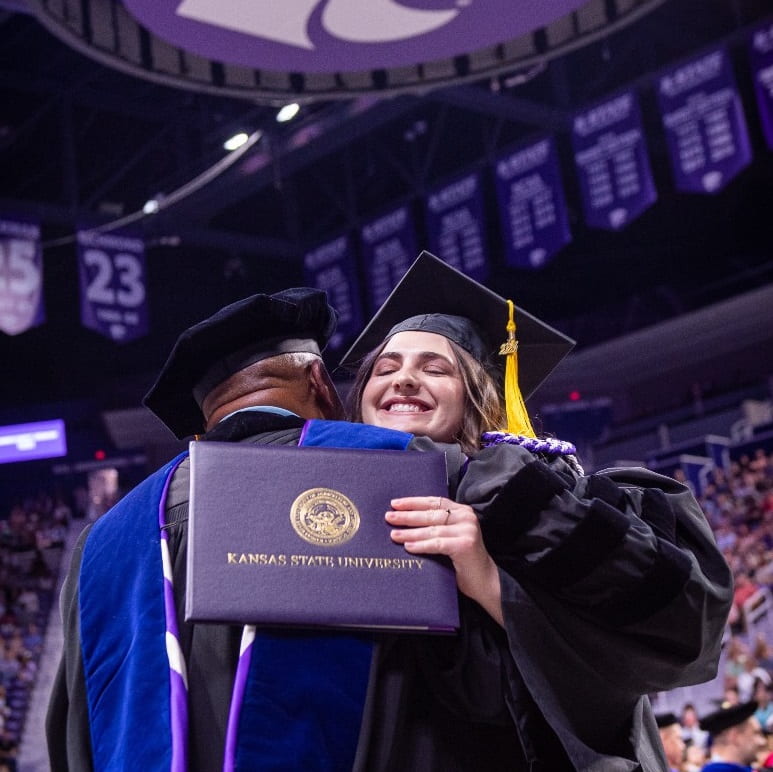 Photo of young woman holding diploma cover and hugging a professor