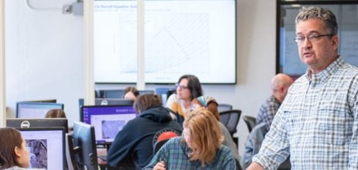 students at computers showing maps and instructor looking on