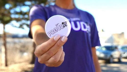 photo of blurry, faceless student holding a Proud button out for viewing