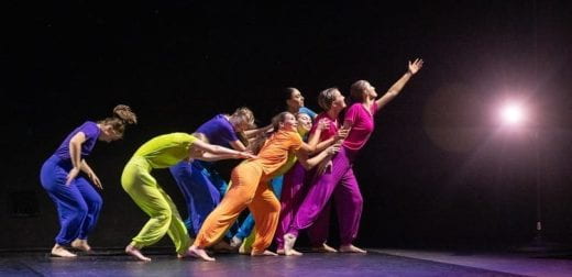 colorfully dressed dancers on stage with black backdrop