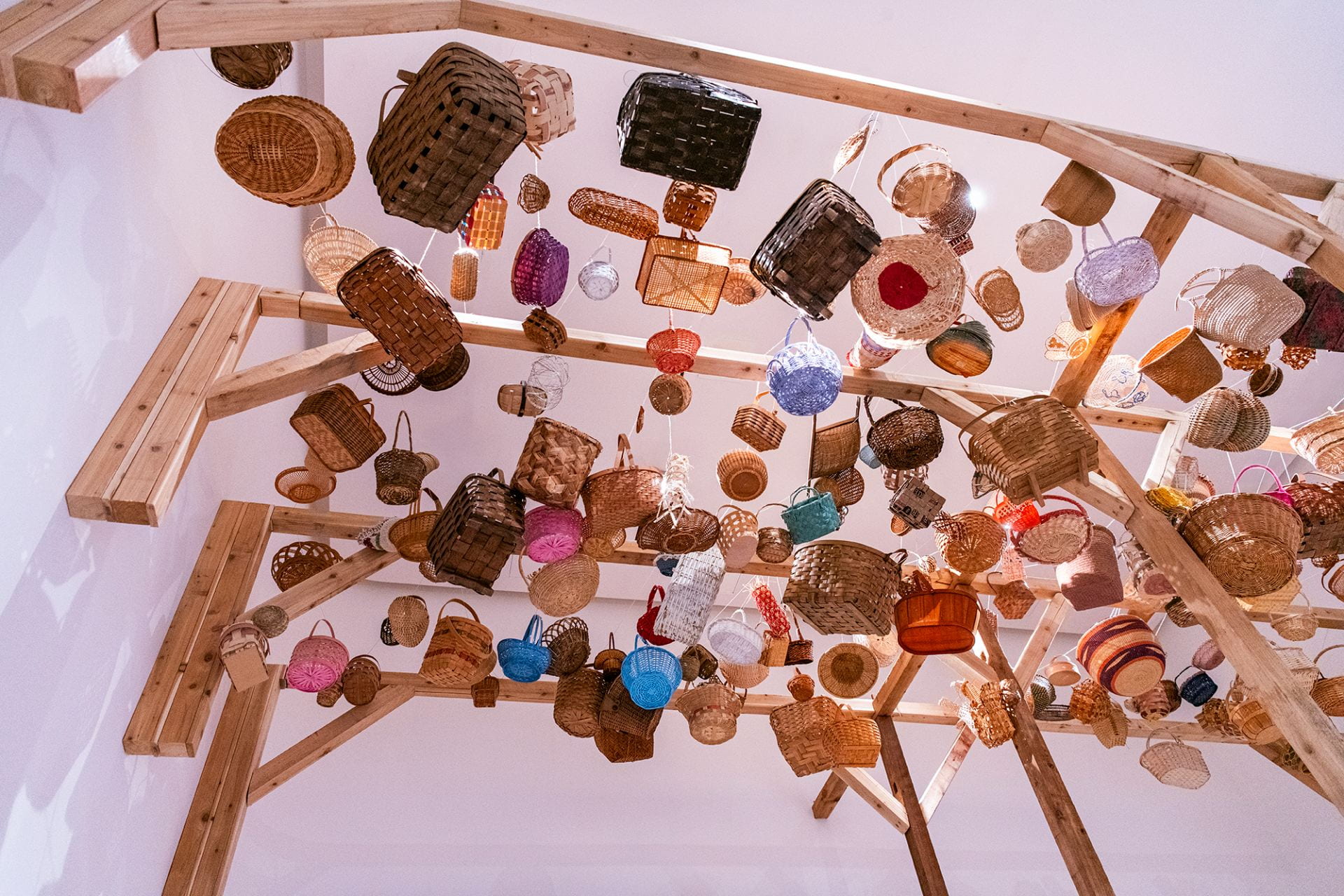 "Woven" by Poppy DeltaDawn, a variety of woven cedar and textile baskets hung from a tall wooden structure