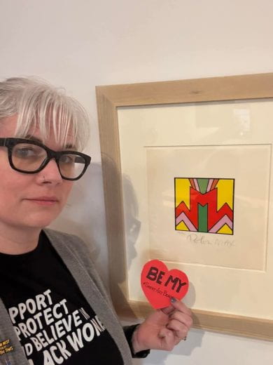 Beach SweetART contest participant holding a paper heart in front of a favorite artwork on display at the Beach Museum of Art.