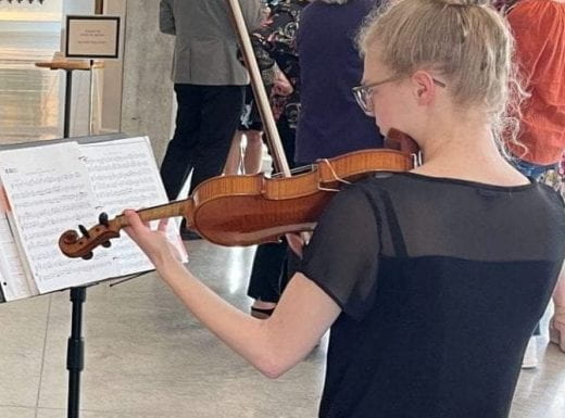 A reception at the Beach Musuem of Art with guests socializing in the atrium and students playing string instruments like violin and cello.