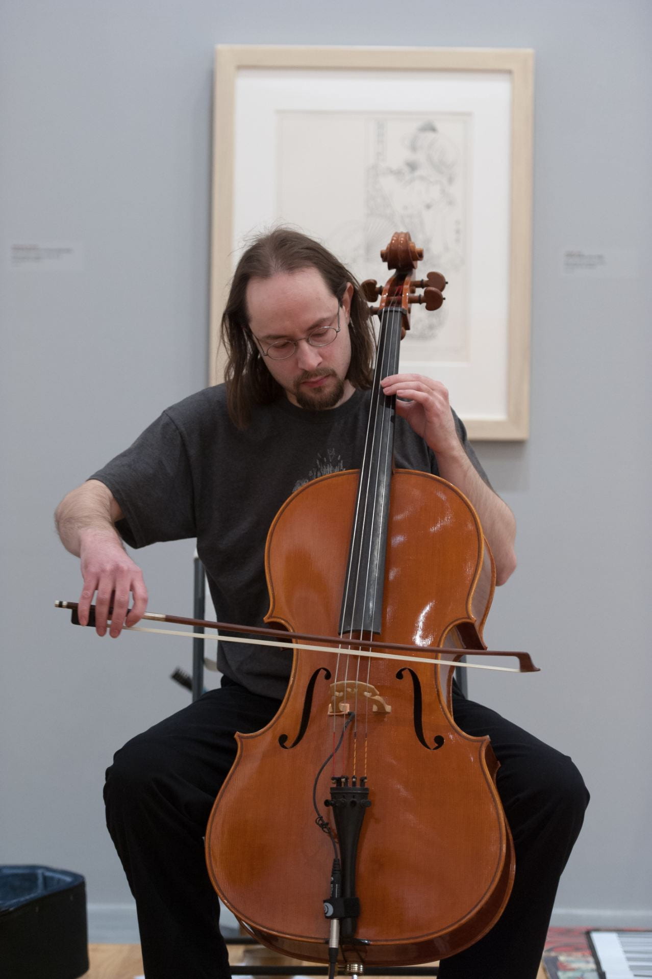 A cellist playing cello in one of the Beach Museum of Art galleries with art displayed on walls in the background. 