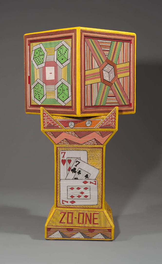 A cube like sculpture and pedestal made from joining corrugated cardboards and painted patterns over it.