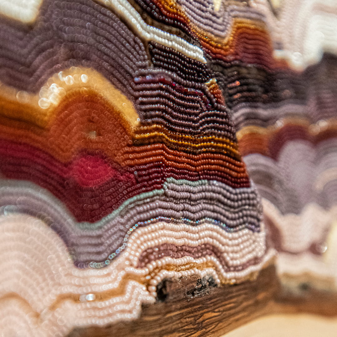 Several tiny beads stuck together in rows on an uneven surface to create a topographical sculptural work.