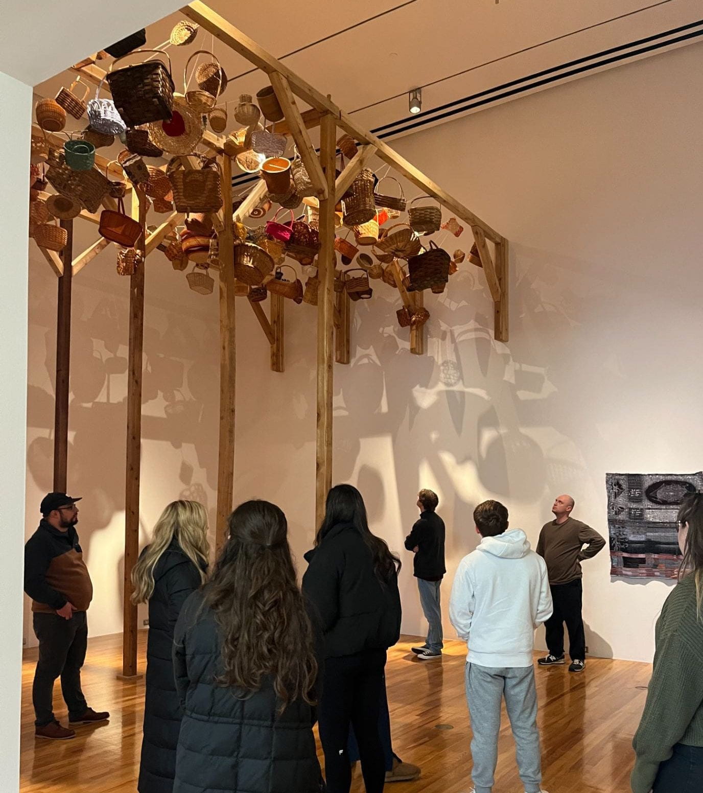 "Woven" by Poppy DeltaDawn, a variety of woven cedar and textile baskets hung from a tall wooden structure