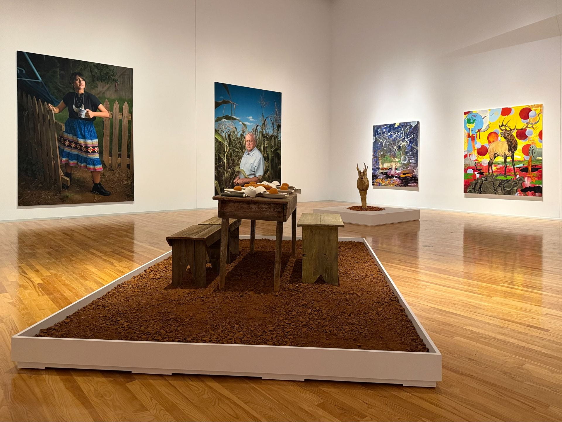 Sculptures and wall paintings and photographs displayed in a gallery at the Beach Museum of Art.
