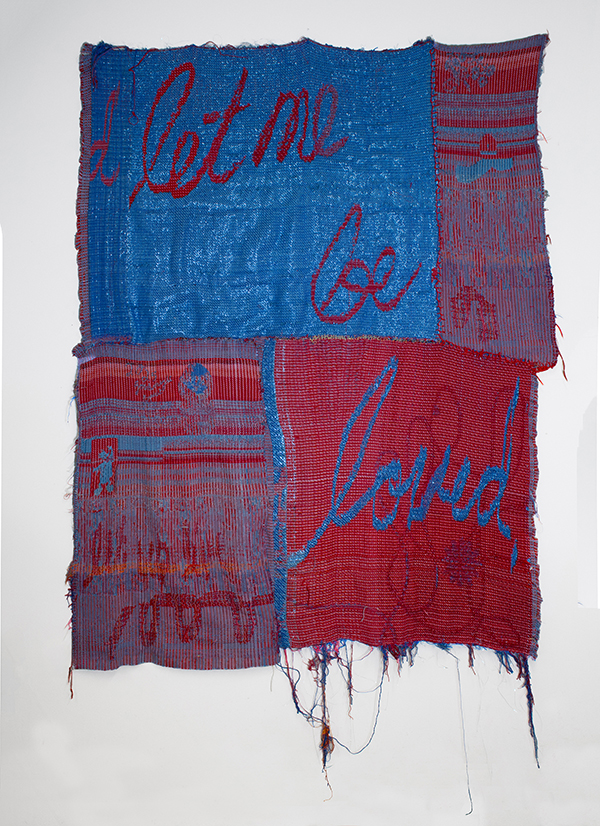 A piece of art in woven fabric with alternating red and blue blocks with the words let me be loved on it.