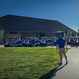 Back of Willie the Wildcat mascot looking at golf carts at golf course