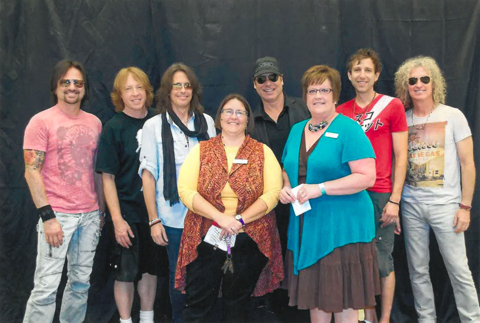 A group of rockstars pose for a group photo around a woman in the center.