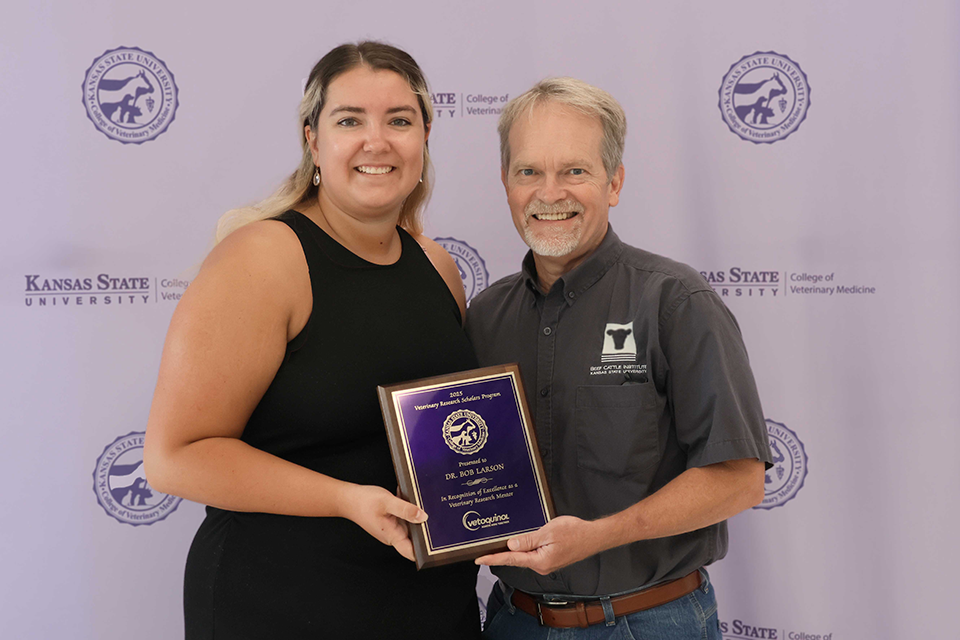 A student stands with her mentor while holding up an award.