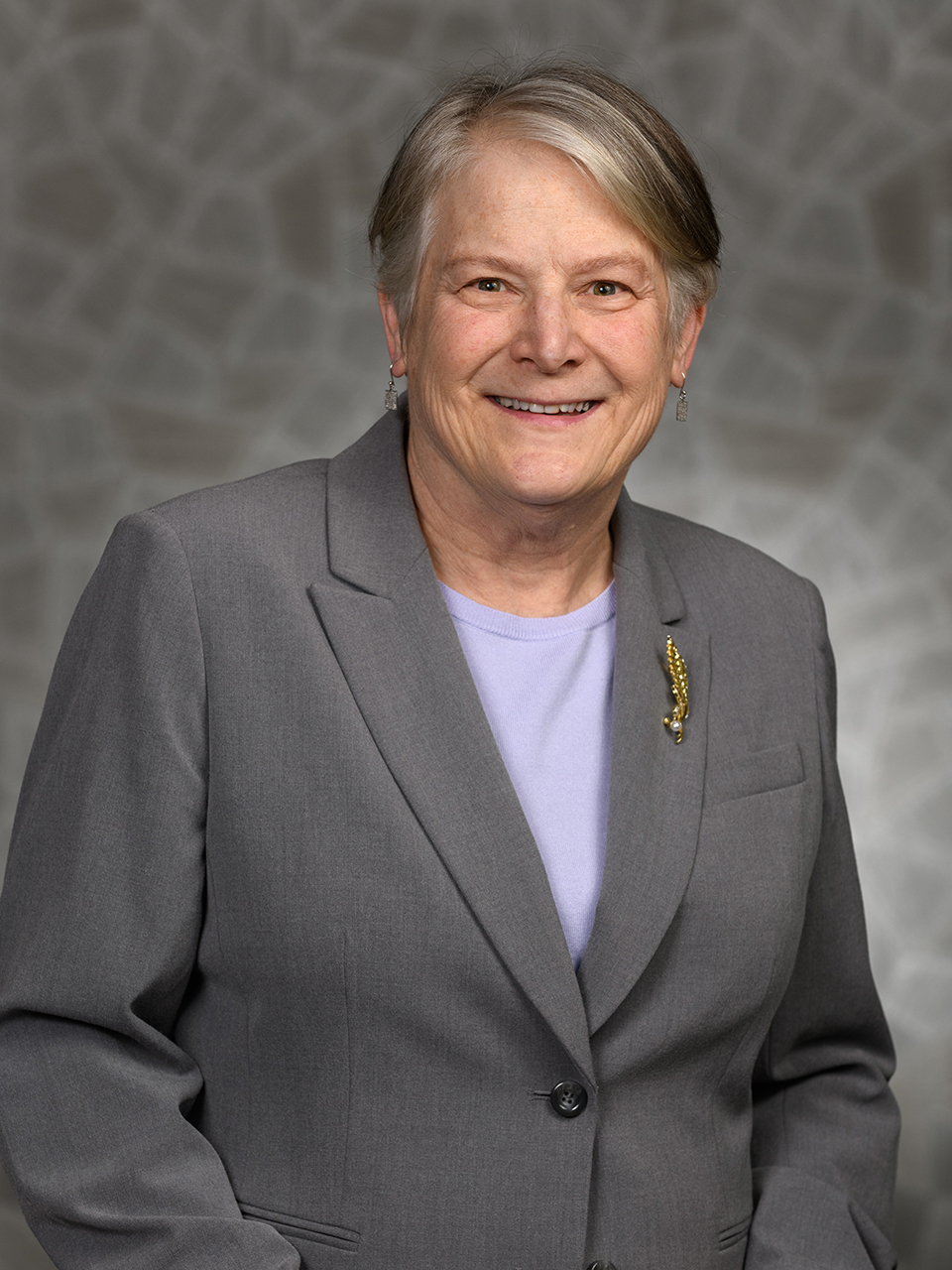 A woman in a gray blazer poses for a portrait in front of a blurred gray background.