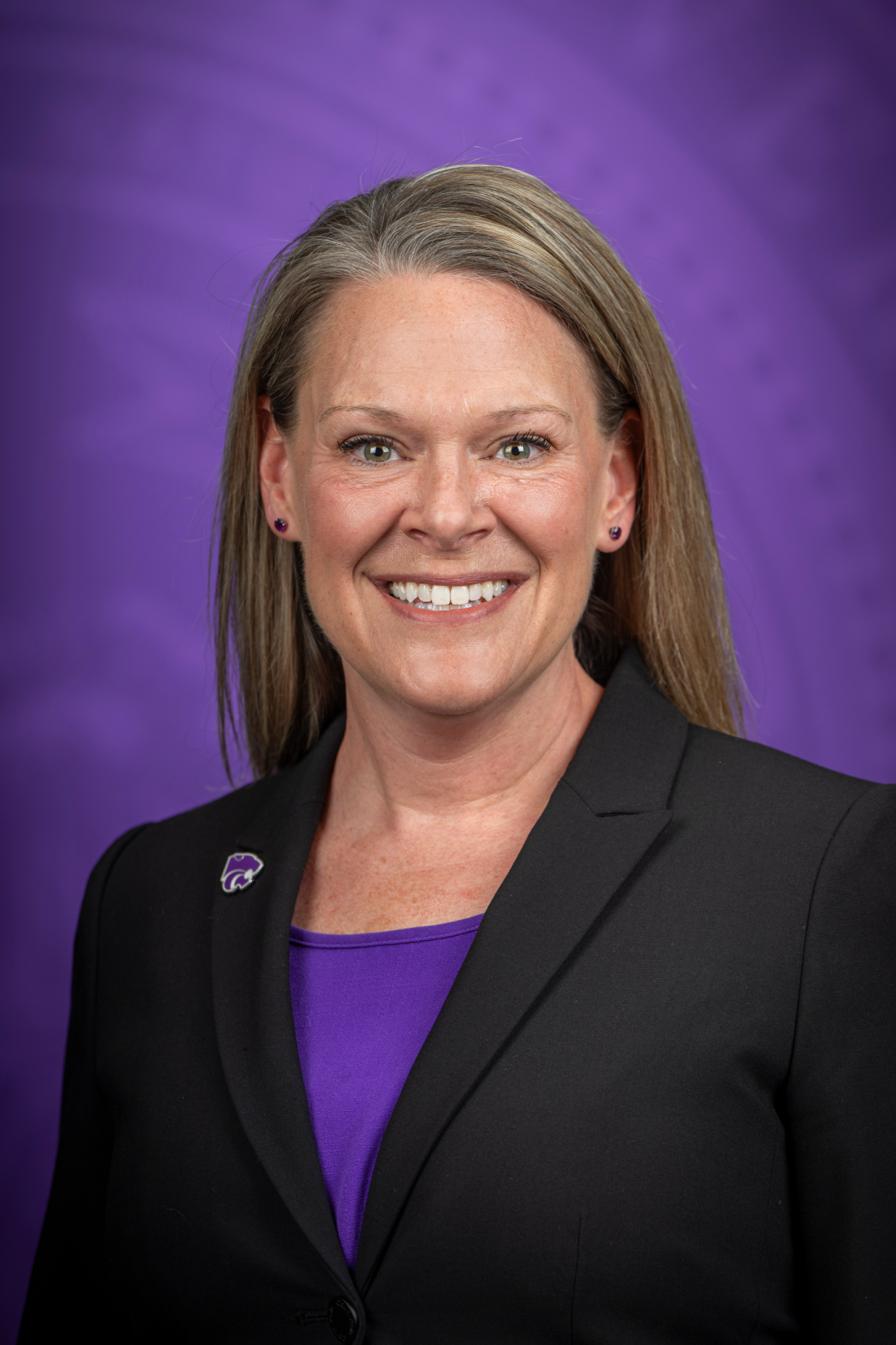 Susan Metzger poses for a portrait with the Kansas State University seal in purple and out of focus behind her.