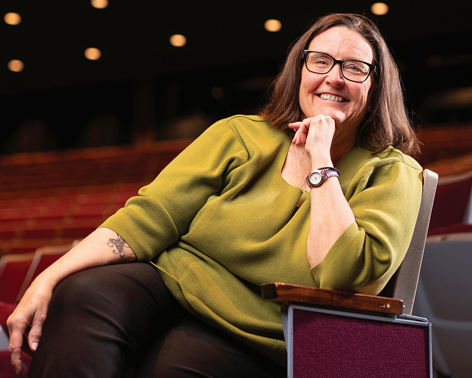 A woman in green shirt leans back in chair and smiles for a portrait.