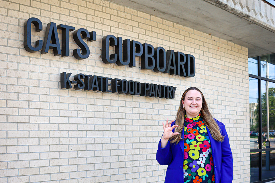 A woman in a floral shirt and purple blaser stand outside of a limestone building that says "Cats Cupboard.".