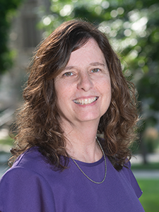  A woman with brown, shoulder-length hair wears a purple blouse and poses for a portrait.