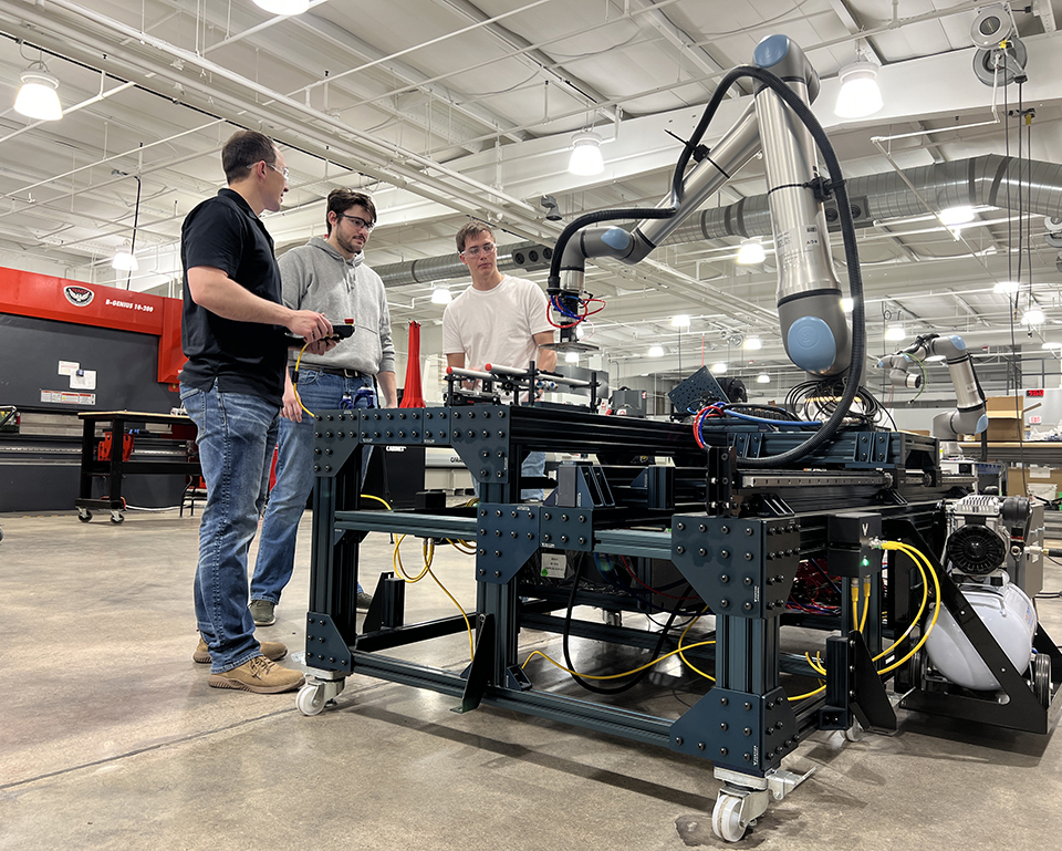 An instructor and a student work on an industrial machine inside a warehouse.