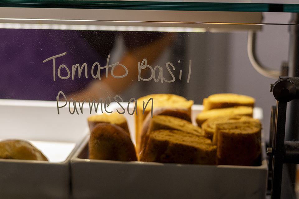 Several loaves of sliced bread sit behind a glass case that says "Tomato basil."