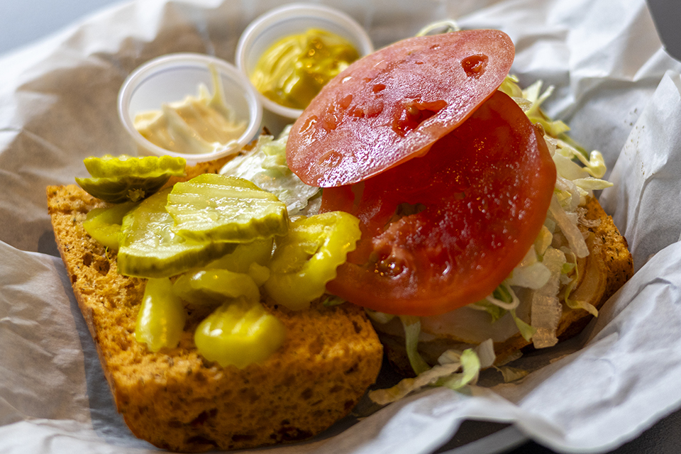 An open-faced sandwich shows special grain bread and tomatoes, pickles and mustard.