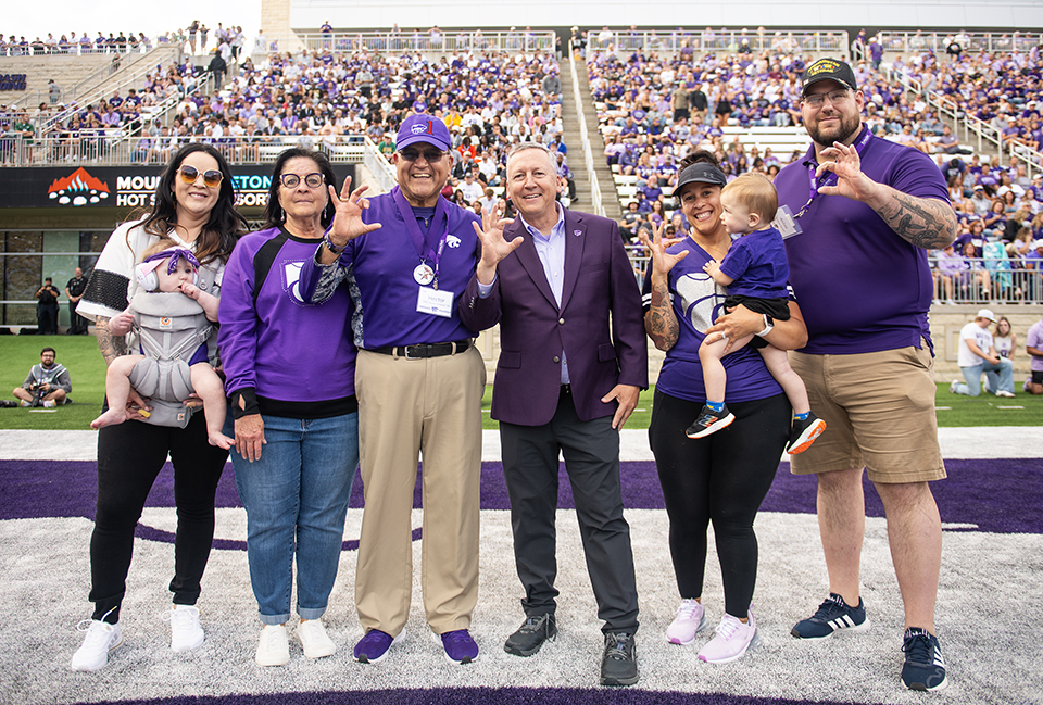 A military veteran and a university president, joined by the veteran's family, pose for a group portrait on a stadium's football field.