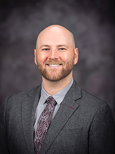 Benjamin Reiswig wears a dark gray suit and smiles for a portrait. 