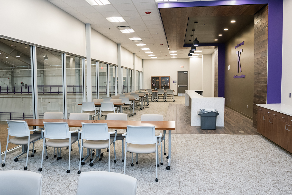A room of chairs and tables that overlooks an indoor rodeo arena