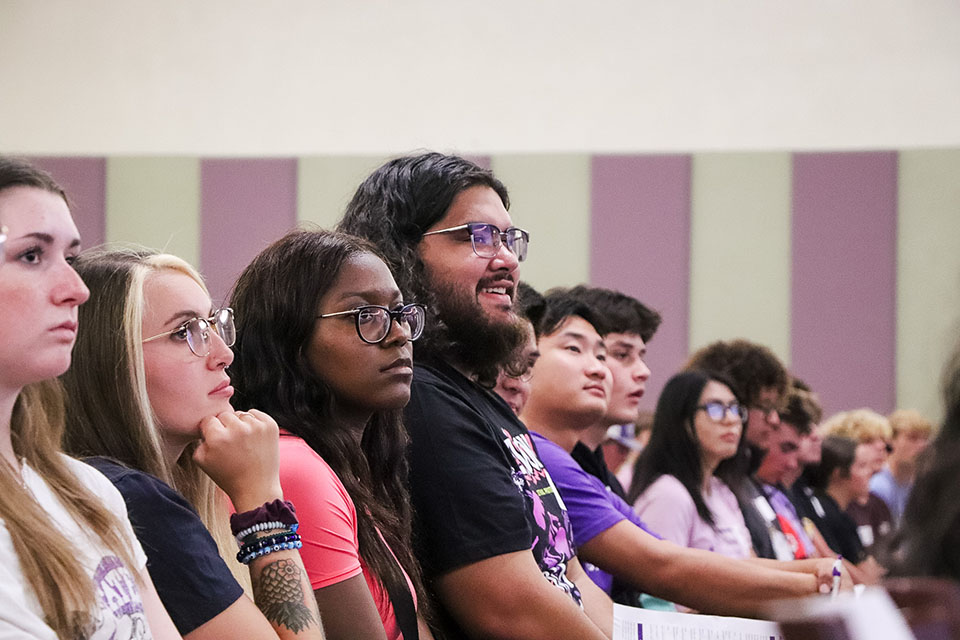 A group of students sit in a crowd and watch a speaker.